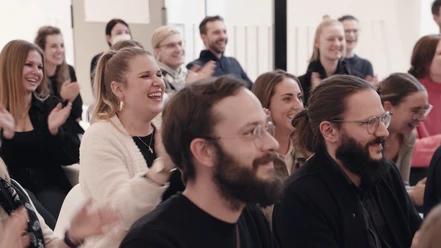Jazzunique GmbH Women and men sit in rows, laughing and clapping enthusiastically.