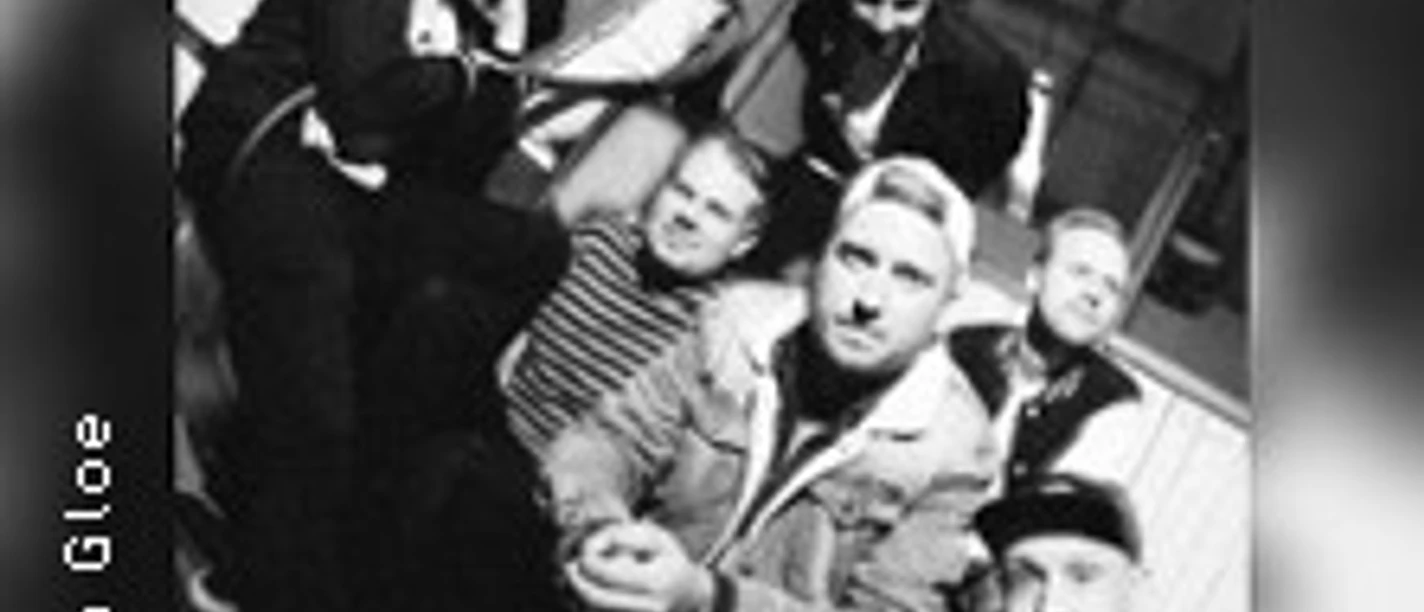 Eine Band posiert lässig in einem Gebäude mit großer Fensterfront im Hintergrund, Schwarz-Weiß-Foto.