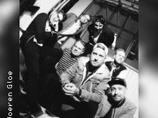 Eine Band posiert lässig in einem Gebäude mit großer Fensterfront im Hintergrund, Schwarz-Weiß-Foto.