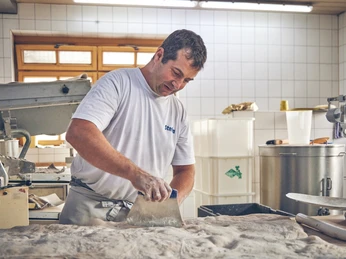 Bäckerei Luidl Bäcker in Arbeitskleidung knetet Teig in heller, gefliester Backstube.