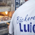 Bäckerei Luidl Bäcker in Luidl-T-Shirt nimmt frisch gebackenes Brot aus dem Ofen.