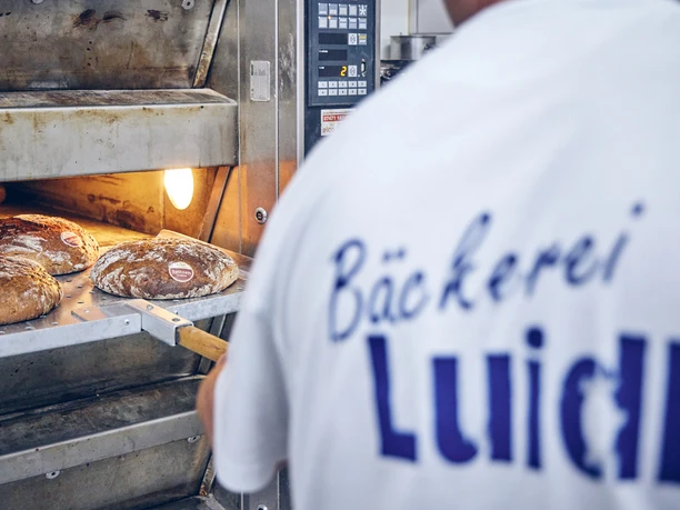 Bäckerei Luidl Bäcker in Luidl-T-Shirt nimmt frisch gebackenes Brot aus dem Ofen.