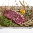 Murnau-Werdenfelser-Rind Ein Stück rohes Rindfleisch liegt auf Stroh, umgeben von frischen Kräutern und Getreide.