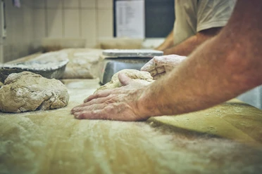 Bäckerei Sand Bäckerhände kneten Teig auf einer bemehlten Arbeitsfläche.