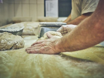Bäckerei Sand Bäckerhände kneten Teig auf einer bemehlten Arbeitsfläche.