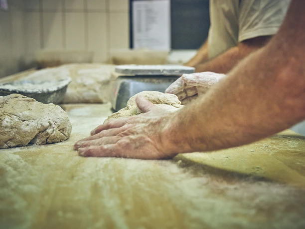 Bäckerei Sand Bäckerhände kneten Teig auf einer bemehlten Arbeitsfläche.