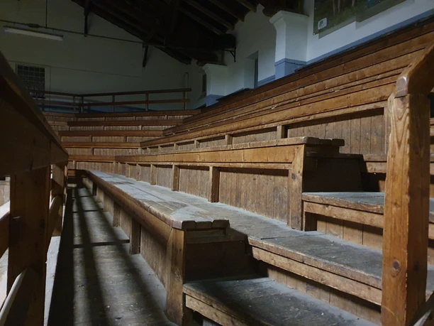 Holzbestuhlte Auktionshalle bei Tageslicht, leere Sitzbänke mit Fokus auf die Architektur.