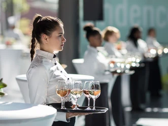 Accente Gastronomie Service GmbH Service staff lined up with trays full of aperitif glasses in their hands.