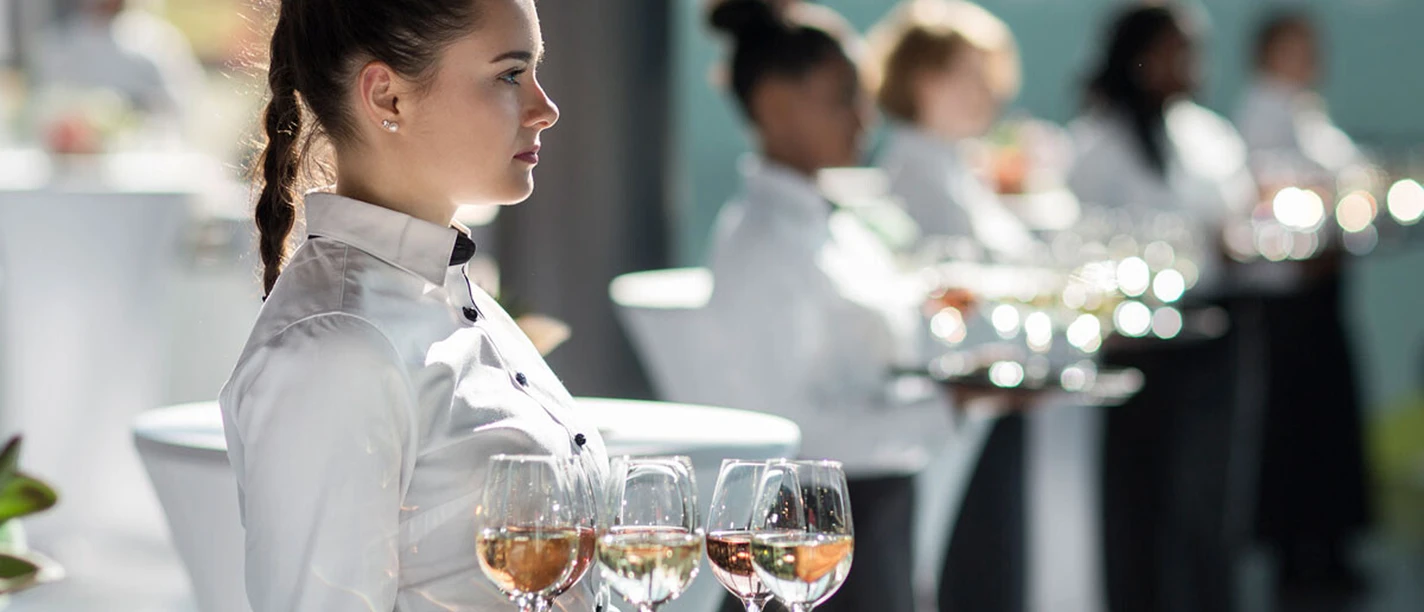 Accente Gastronomie Service GmbH Service staff lined up with trays full of aperitif glasses in their hands.