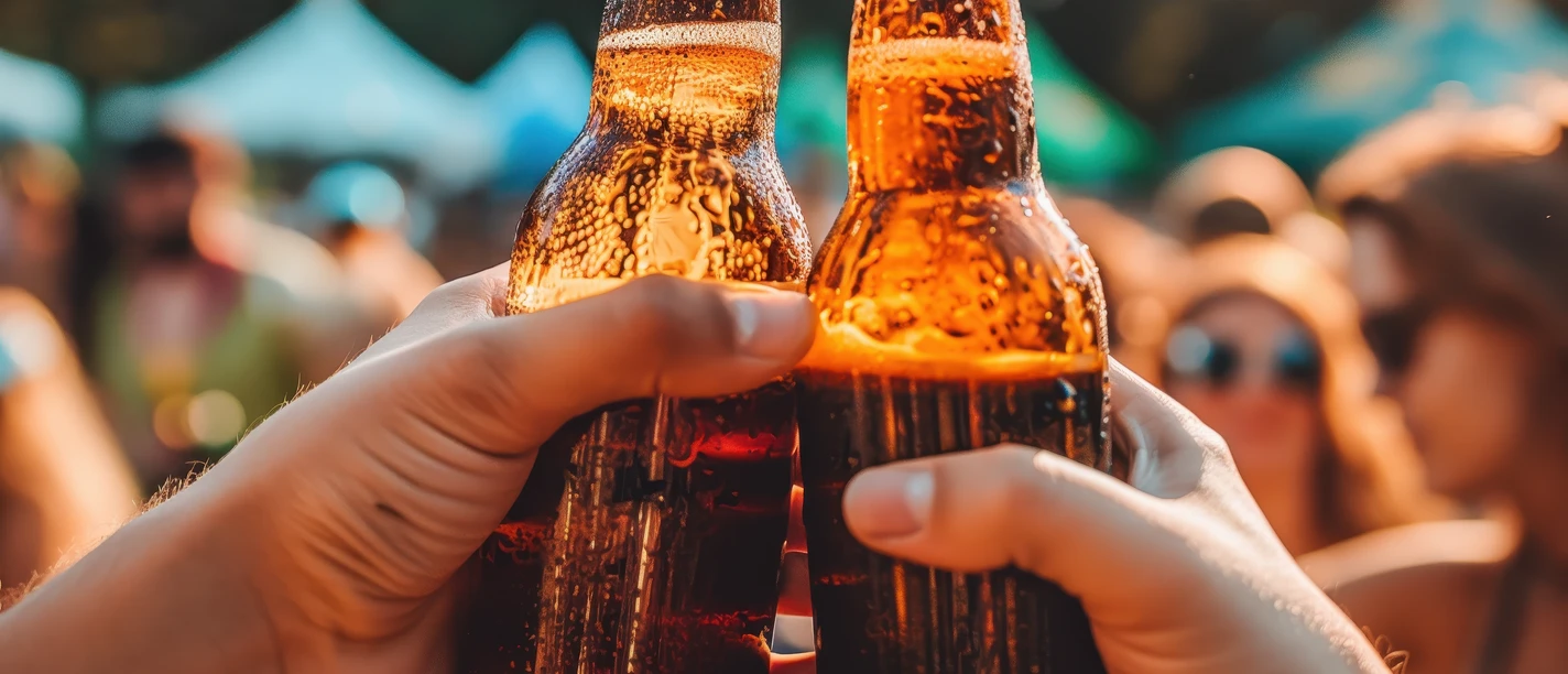 Bierfest Greetsiel Zwei Bierflaschen, die anstoßen. Im Hintergrund feiernde Menschen.