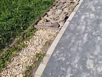 Barfusspfad Hennesee Kiesel Das Bild zeigt einen Barfußpfad mit verschiedenen Texturen: Gras, Kieselsteine und größere Steine. Der Pfad windet sich in einer sanften Kurve. Im Hintergrund sind grüne Pflanzen sichtbar.
