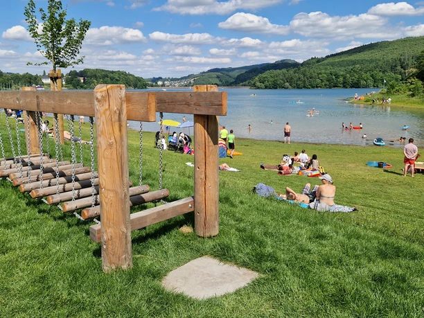Barfusspfad Hennesee Wackelbrücke Auf dem Bild ist ein lebendiger Barfußpfad am Hennesee zu sehen. Menschen entspannen auf der Wiese.