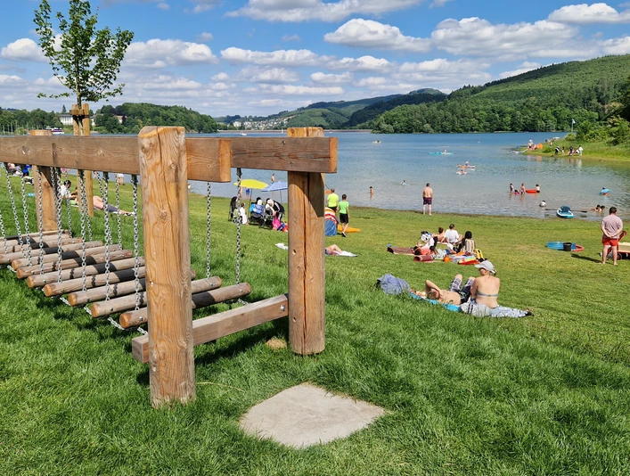 Barfusspfad Hennesee Wackelbrücke Auf dem Bild ist ein lebendiger Barfußpfad am Hennesee zu sehen. Menschen entspannen auf der Wiese.