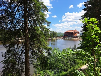 Blick durch Bäume auf den Mummelsee mit Berghotel vor blauem Himmel mit Wolken