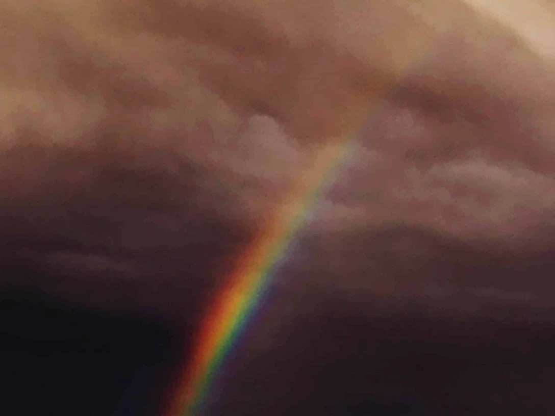 Ein leuchtender Regenbogen durchbricht dunkle, dramatische Wolken am Himmel.