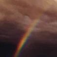 Ein leuchtender Regenbogen durchbricht dunkle, dramatische Wolken am Himmel.