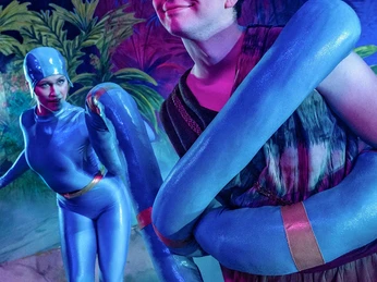 Dschungelbuch - das Musical 1 (c) Theater Liberi.jpg Ein Schauspieler in einem bunten Outfit wird von einer blauen Schlange um die Schultern eingewickelt.