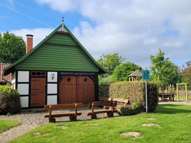 Ortsteil Stockausen Lübbecke Fachwerkhaus mit grünem Giebel, Spielplatz im Hintergrund, Bänke und Hecken im Vordergrund.