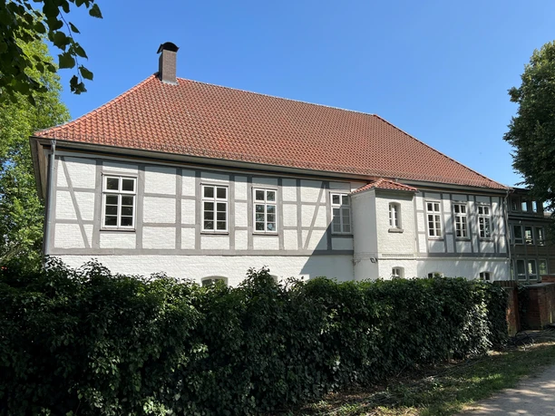 Fachwerkaus Haus unter blauem Himmel, umgeben von grünen Bäumen und Hecken, klar und hell.