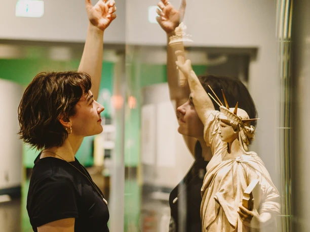 Freiheit 4_Isabel Noack.jpg Frau betrachtet fasziniert ein Modell der Freiheitsstatue hinter Glas in einem Museum.