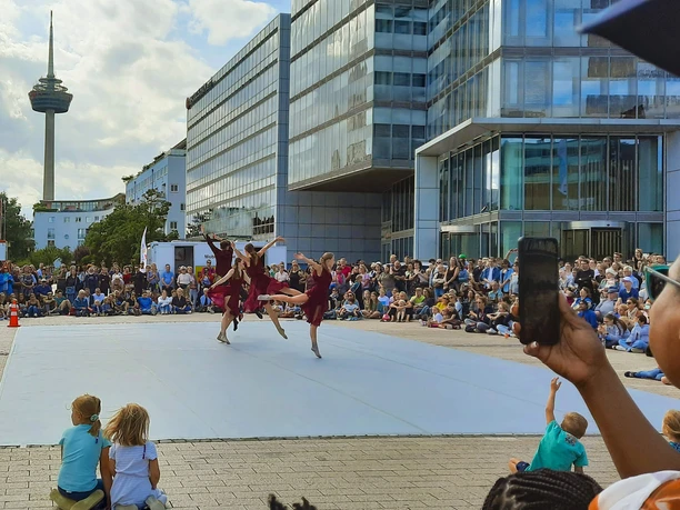 KölnTanz at the Open Air Summer Cologne Four dancers perform a modern choreography on an open-air stage in urban Cologne, surrounded by a fascinated audience.