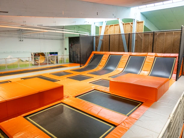 Große Trampolinhalle mit bunten Sprungfeldern und gepolsterten Wänden für sicheres Spielen.