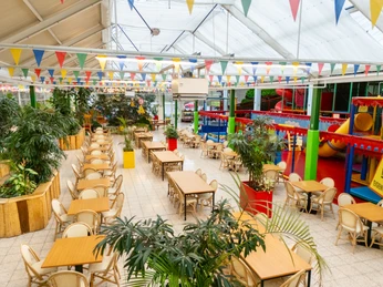 Große Indoor-Spielhalle mit bunten Spielgeräten, langen Tischreihen und farbenfrohen Wimpeln.