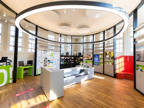 Moderne Touristeninformation mit interaktiven Displays, Infomaterial und bequemen Sitzgelegenheiten.