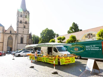 herford-markt-teutoburger-wald-tourismus-h-tornow-009-jpg.jpg Ein Marktplatz mit einem Verkaufsstand voller frischer Produkte, umgeben von historischen Gebäuden.