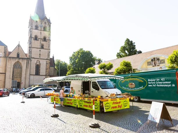 herford-markt-teutoburger-wald-tourismus-h-tornow-009-jpg.jpg Ein Marktplatz mit einem Verkaufsstand voller frischer Produkte, umgeben von historischen Gebäuden.