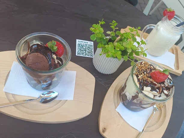 Twee desserts met chocolade en aardbeien op houten plankjes, vergezeld van een drankje in een glas.