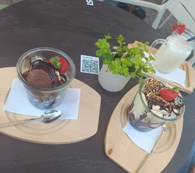 IMG_20250619_112143649.jpg Zwei Desserts mit Schokolade und Erdbeeren auf Holzbrettern, begleitet von einem Getränk im Glas.