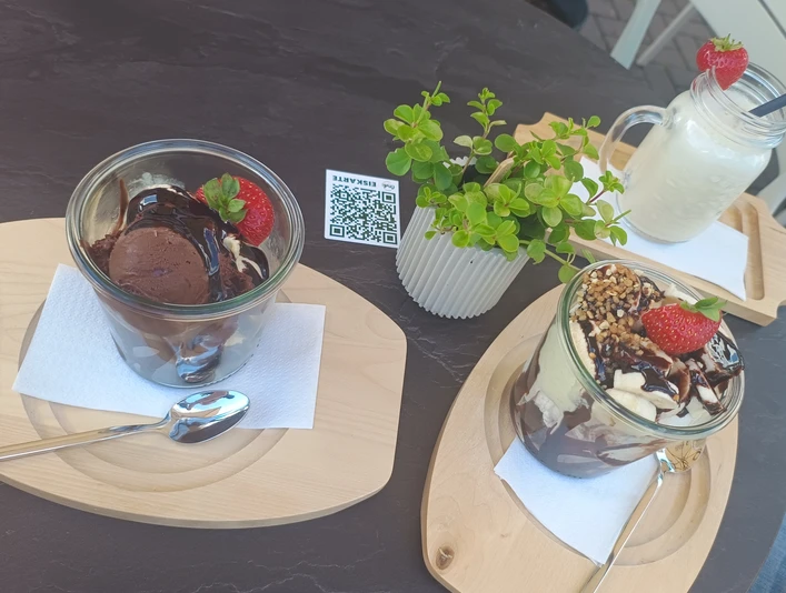 IMG_20250619_112143649.jpg Zwei Desserts mit Schokolade und Erdbeeren auf Holzbrettern, begleitet von einem Getränk im Glas.