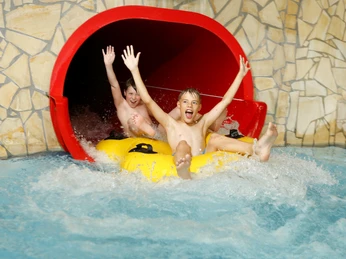 Freizeitbad-Freizeiteinrichtungen Stadtwerke Herford GmbH.JPG Zwei Kinder rutschen vergnügt auf einem gelben Reifen aus einer Wasserrutsche in ein Schwimmbecken.