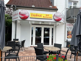 Euphrat.jpg Der Eingang wird vorne mit Tischen und Stühlen zum Sitzen geschmückt und das Logo "Euphrat" in gelb mit einem roten Schriftzug ist vorne direkt über der Tür platziert.