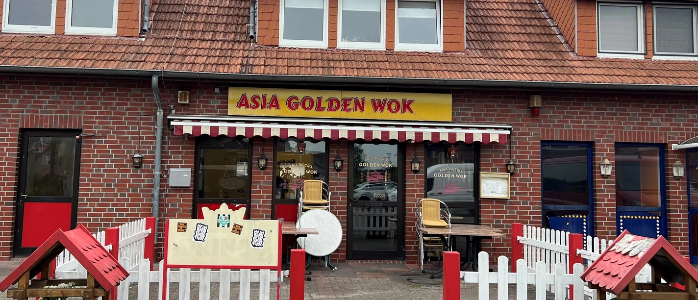 Golden Wok.jpg Das Bild zeigt das Restaurant Asia Golden Wok, ein Backsteingebäude mit roten Dachziegeln. Vor dem Eingang gibt es weiße und rote Absperrungen, Blumenhäuschen und eine Speisekarte.