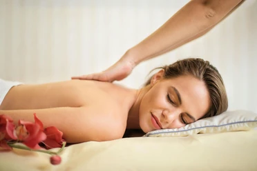 Bad-Driburg Biomaris Beautyoase Eine Frau genießt eine Rückenmassage auf einem bequemen Kissen, neben ihr eine rote Blume.
