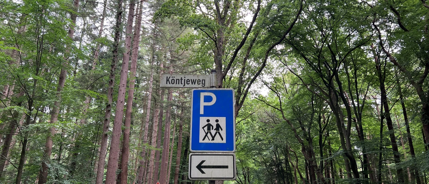 Kötnjeweg1.jpg Ein blaues Verkehrsschild zeigt einen Parkplatz an, umgeben von einem Wald am Kötnjeweg.
