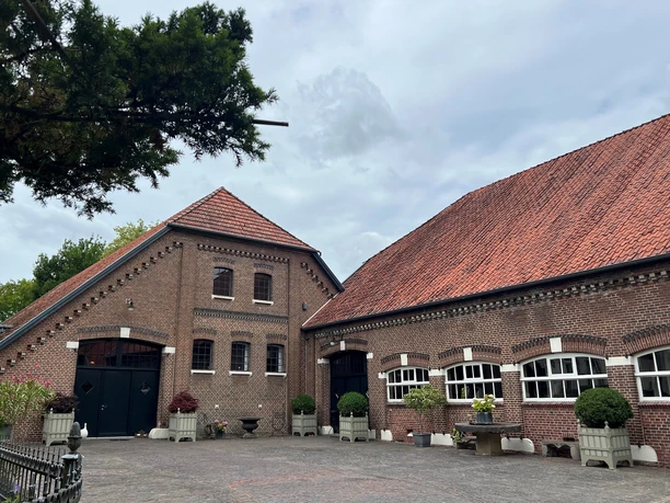 Bild6.jpg Ein großer, roter Ziegelbau mit Krüppelwalmdach und mehreren Fenstern bildet einen Hof.