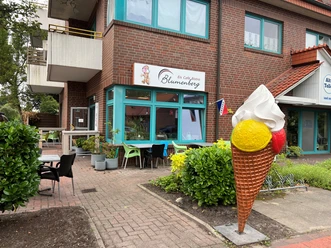 EisCafe Blumenberg.jpg Vor einem Backsteingebäude steht eine große bunte Eiswaffel-Skulptur. Davor sind Sitzgelegenheiten und Pflanzen.
