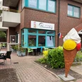 EisCafe Blumenberg.jpg Vor einem Backsteingebäude steht eine große bunte Eiswaffel-Skulptur. Davor sind Sitzgelegenheiten und Pflanzen.