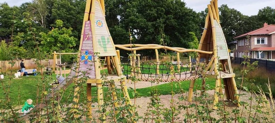 Spielplatz Marienbader Straße Ein lebhafter Spielplatz mit hölzernen Klettergeräten, Seilbrücke und fröhlichen Farben, umgeben von grüner Vegetation. Ideal für Kinder, um sich auszutoben und die Natur zu genießen.