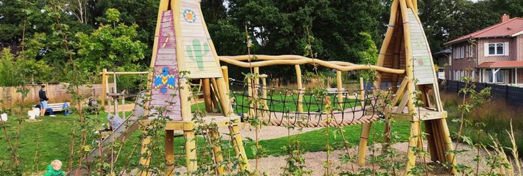 Spielplatz Marienbader Straße Ein lebhafter Spielplatz mit hölzernen Klettergeräten, Seilbrücke und fröhlichen Farben, umgeben von grüner Vegetation. Ideal für Kinder, um sich auszutoben und die Natur zu genießen.