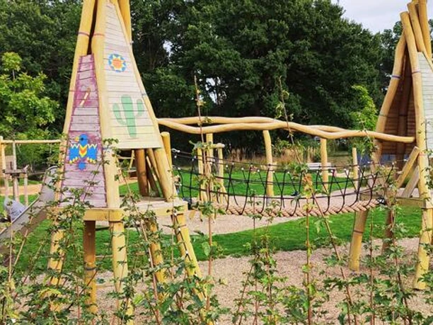 Spielplatz Marienbader Straße Ein lebhafter Spielplatz mit hölzernen Klettergeräten, Seilbrücke und fröhlichen Farben, umgeben von grüner Vegetation. Ideal für Kinder, um sich auszutoben und die Natur zu genießen.