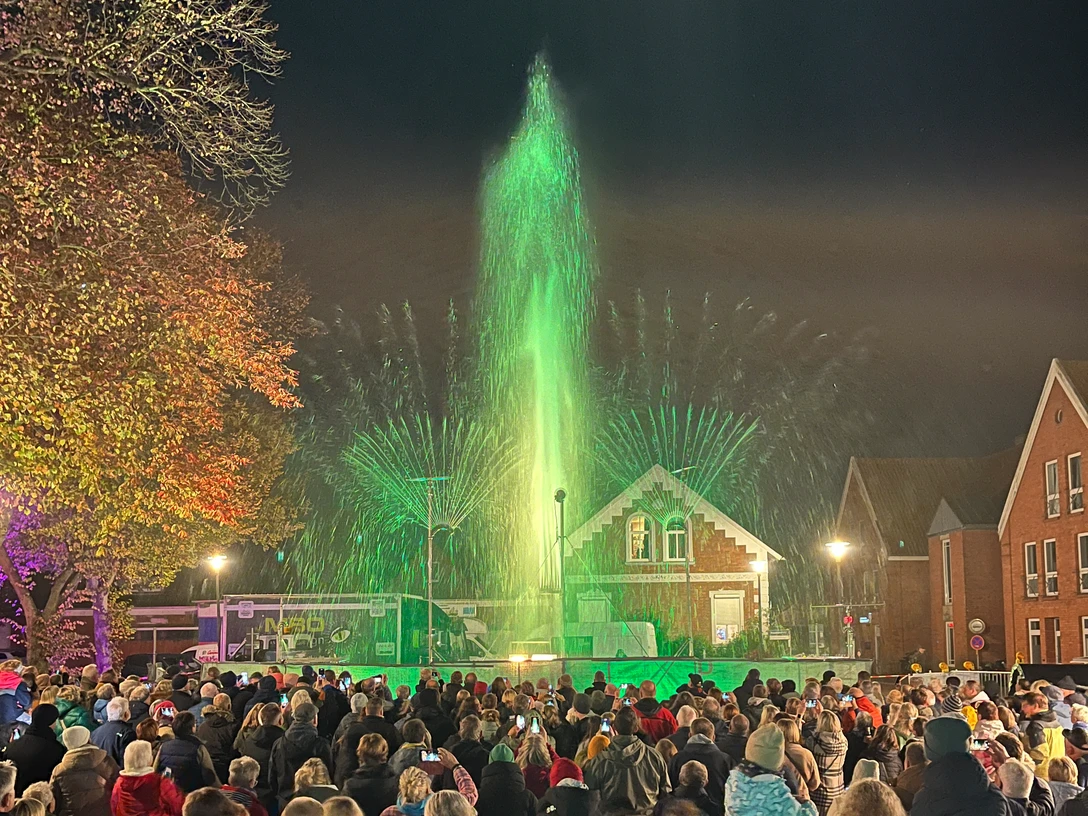 Flames of Water 2024 Menschenmenge beobachtet abends eine grün beleuchtete Wasser- und Lichtshow vor historischen Gebäuden