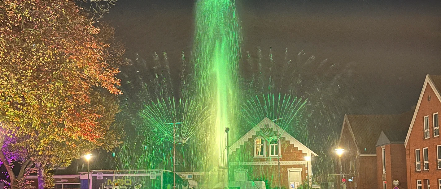 Flames of Water 2024 Menschenmenge beobachtet abends eine grün beleuchtete Wasser- und Lichtshow vor historischen Gebäuden