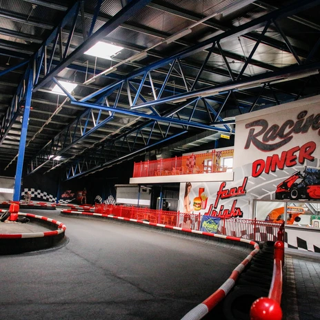 Funpark Meppen - Indoor-Kartbahn 02 © Emsland Tourismus GmbH.jpg Innenansicht einer hell beleuchteten Indoor-Kartbahn mit rot-weißer Streckenbegrenzung und Tribüne.