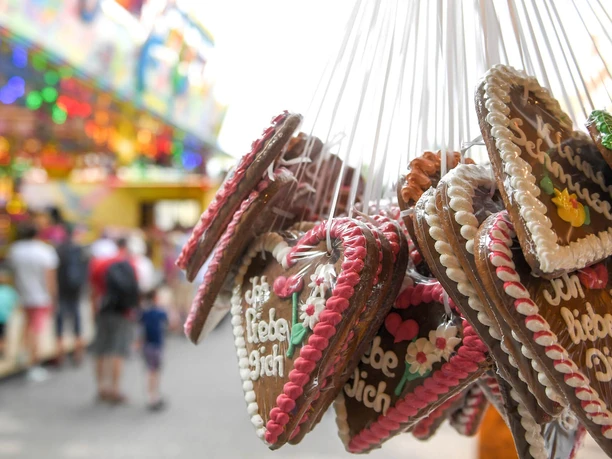 Saarner Kirmes (2017), Mülheim an der Ruhr Lebkuchenherzen mit der Aufschrift "Ich liebe Dich" hängen an Schnüren vor einem bunten Kirmeshintergrund.
