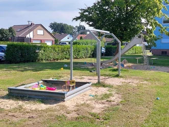 Spielplatz Bartensteiner Weg Spielplatz mit Rutsche, Sandkasten und grünem Rasen, umgeben von Wohnhäusern und Hecken.