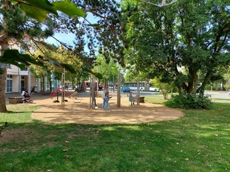 Ein Spielplatz mit Klettergerüsten und Spielgeräten, umgeben von Bäumen im grünen Park.